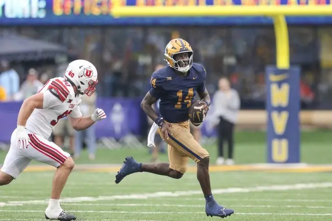 Sep 27, 2025; Morgantown, West Virginia, USA; West Virginia Mountaineers quarterback Khalil Wilkins (14) runs away from Utah Utes defensive end John Henry Daley (90) during the third quarter at Milan Puskar Stadium. Mandatory Credit: Ben Queen-Imagn Images